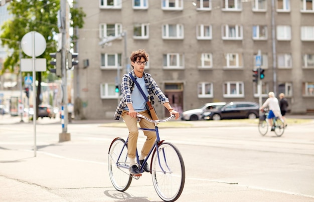 gente, estilo, ocio y estilo de vida - joven hipster con bandolera montando bicicleta fija en la calle de la ciudad