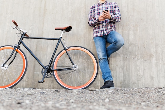 gente, estilo, tecnología, ocio y estilo de vida: cerca de un joven hipster con auriculares con teléfono inteligente y bicicleta fija escuchando música en la calle de la ciudad