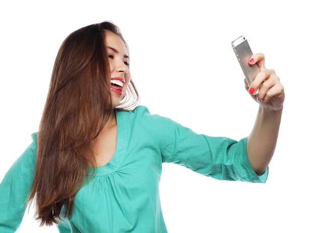 Gente estilo de vida y concepto de tecnología chica adolescente bonita con camisa verde tomando selfies con su teléfono inteligente aislado en blanco