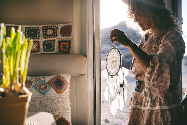 Gente de estilo de vida Wanderlust Una mujer sosteniendo la decoración dreamcather en la puerta de su casa móvil con el aire libre y el atardecer fuera Concepto de vanlife y libertad Vida feliz mujer independiente