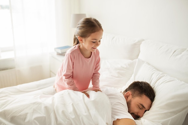 gente, familia y concepto matutino - niñita feliz despertando a su padre dormido en la cama en casa