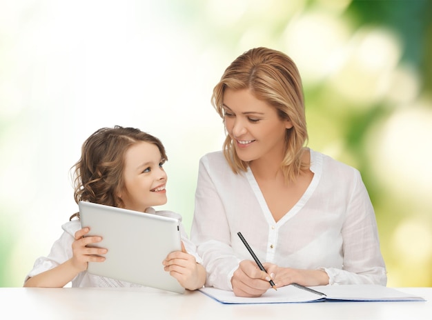 gente, familia, educación en el hogar, concepto de niños y tecnología - feliz madre e hija con tablet pc y portátil sobre fondo verde