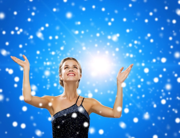 Foto gente, felicidad, vacaciones y concepto de navidad - mujer sonriente levantando la mano y mirando hacia arriba sobre fondo azul nevado