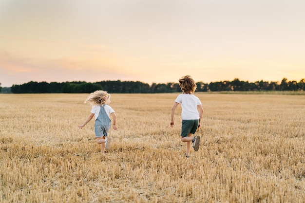 Gente feliz y libre, los niños corren por el campo biselado de la gente de trigo desde atrás