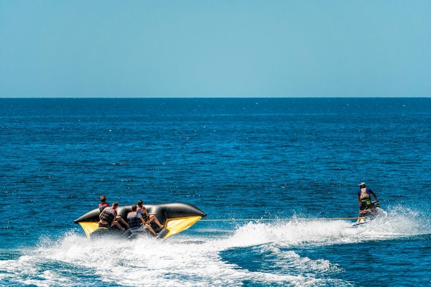 La gente feliz va a nadar en un colchón de aire detrás de una moto de agua, los turistas montan el inflable