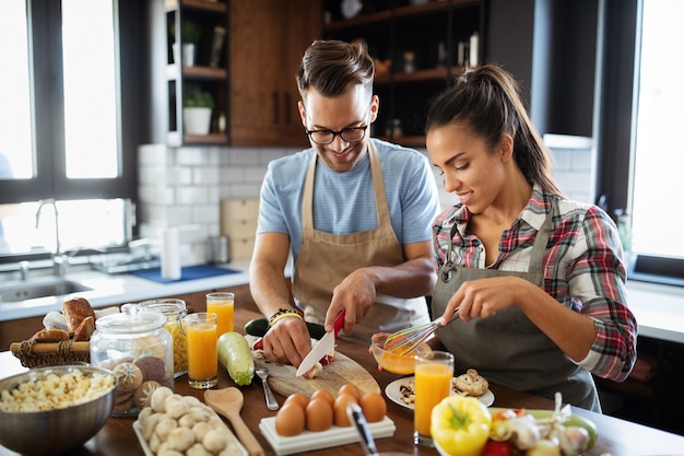 Foto gente feliz, pareja de amigos cocinando juntos en su cocina tipo loft en casa