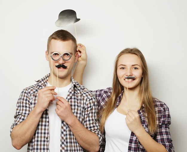 Gente fiesta amor y ocio concepto encantadora pareja sosteniendo gafas de fiesta y bigotes en palos sobre fondo blanco.