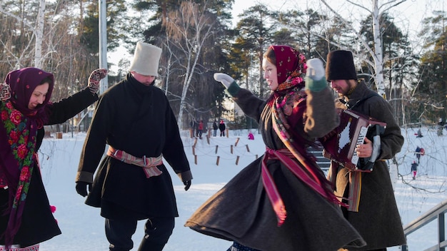 Gente del folclore ruso con botas de fieltro bailando al aire libre en invierno en el parque