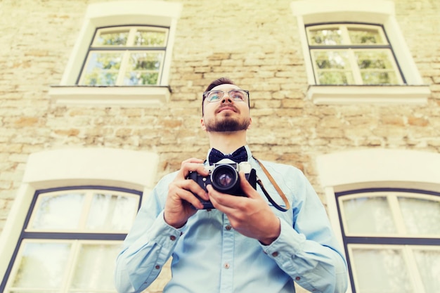 gente, fotografía, tecnología, ocio y estilo de vida - feliz joven hipster con cámara de película retro vintage en la calle de la ciudad