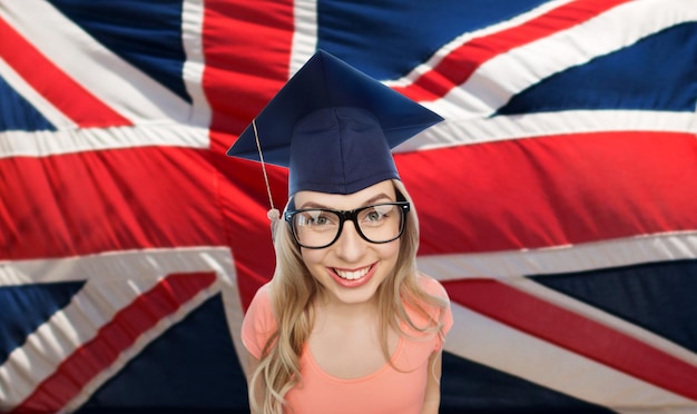 gente, graduación y concepto de educación nacional - joven estudiante sonriente en birrete y anteojos sobre bandera inglesa