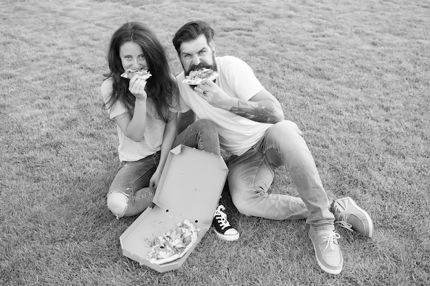 Gente hambrienta Felicidad simple Comida trampa Pareja comiendo pizza relajándose en el césped verde Entrega de comida rápida Hombre barbudo y novia disfrutan de pizza cursi Pareja enamorada saliendo al aire libre con pizza