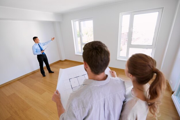 Foto la gente de la hipoteca y el concepto de bienes raíces agente inmobiliario feliz mostrando la ventana en la nueva casa para la pareja con el plano