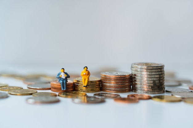 Gente, hombre y mujer en miniatura sentados en monedas de la pila que usan como concepto financiero y comercial