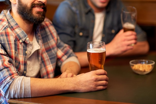 Foto gente, hombres, ocio, amistad y concepto de comunicación - cerca de amigos varones felices bebiendo cerveza de barril en el bar o pub