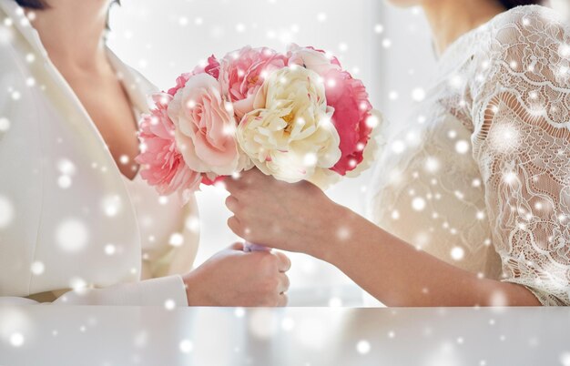 gente, homosexualidad, matrimonio entre personas del mismo sexo y concepto de amor - cerca de una feliz pareja de lesbianas casadas con un ramo de flores sobre el efecto de la nieve