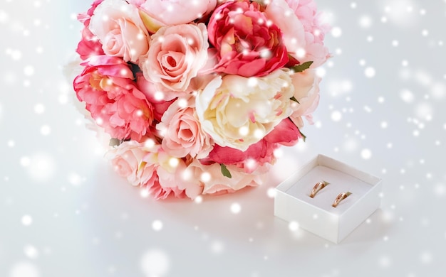 gente, homosexualidad, matrimonio entre personas del mismo sexo y concepto de amor - cierre de anillos de boda gay femeninos en una pequeña caja y ramo de flores en la mesa sobre el efecto de la nieve