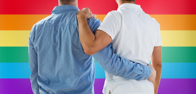 gente, homosexualidad, matrimonio entre personas del mismo sexo, gay y concepto de amor - cerca de una feliz pareja gay masculina o amigos abrazándose desde atrás sobre el fondo de la bandera del arco iris