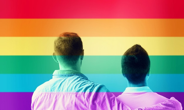 Foto gente, homosexualidad, matrimonio entre personas del mismo sexo, gay y concepto de amor - cerca de una feliz pareja gay masculina o amigos abrazándose desde atrás sobre el fondo de las rayas de la bandera del arco iris