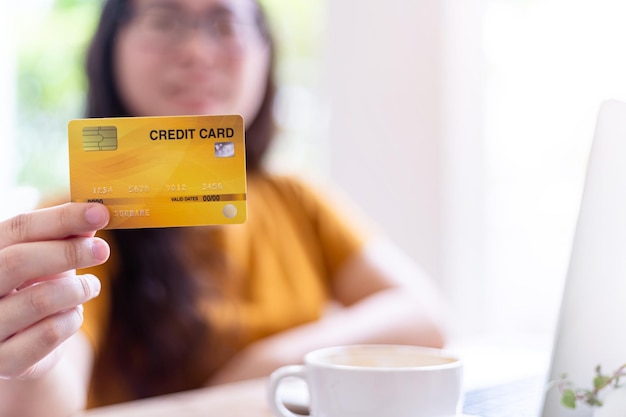 Gente independiente de negocios casual femenino Desenfoque abstracto con enfoque en mostrar sosteniendo una tarjeta de crédito trabajando con una computadora portátil en una cafetería como el fondo para compras y pagos en línea