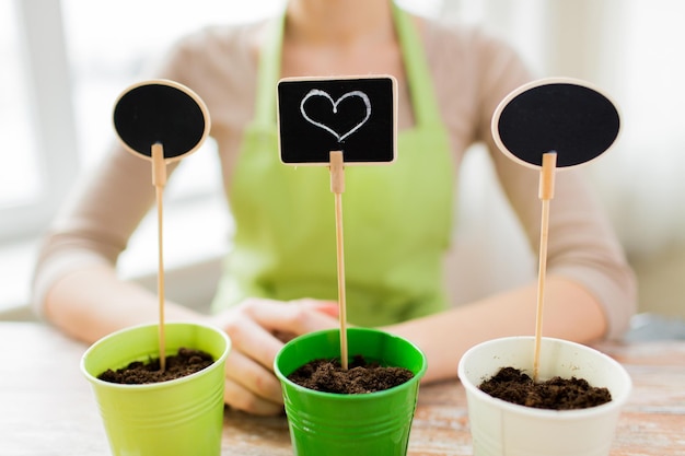 gente, jardinería, siembra, día de san valentín y concepto de vacaciones - cierre de mujer sobre macetas con tierra y carteles