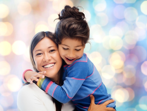 gente, maternidad, familia y concepto de adopción - feliz madre e hija abrazándose sobre el fondo azul de las luces navideñas