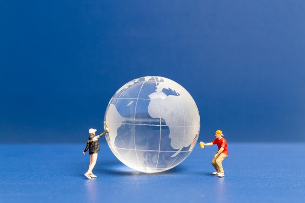 Gente en miniatura Adolescente rociando pintura crytal globo sobre fondo azul Concepto del día mundial del medio ambiente