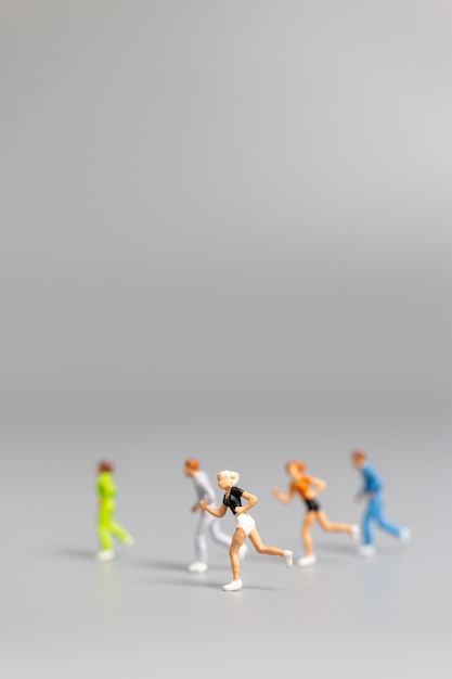 Foto gente en miniatura corriendo sobre fondo gris y espacio libre para texto