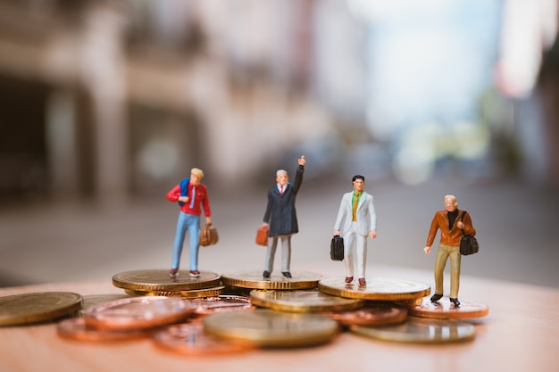 Gente miniatura, equipo de negocios de pie en las monedas de la pila