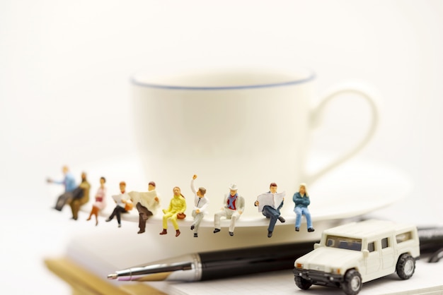 Gente en miniatura: equipo de negocios sentado en una taza de café con noticias de la mañana.