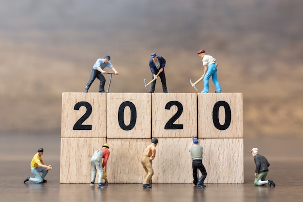 Gente en miniatura: el equipo de trabajadores crea un bloque de madera número 2020