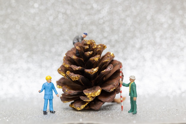 Gente en miniatura con el equipo de trabajadores preparando un cono de pino de Navidad