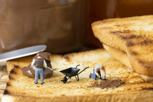 La gente en miniatura está untando chocolate sobre una tostada.