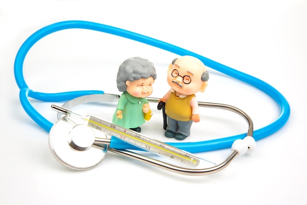 Gente en miniatura Estetoscopio y figuritas de jubilados sobre un fondo blanco El concepto de salud y prevención de enfermedades en los ancianos