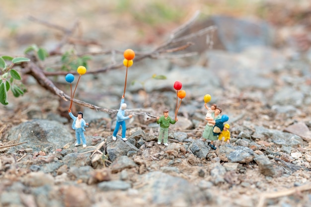 Gente en miniatura: familia feliz caminando en el campo con globos