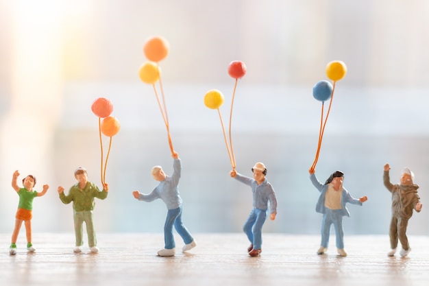 Gente en miniatura: familia feliz caminando con globos