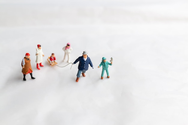 Gente en miniatura Familia feliz monta un trineo con fondo de nieve