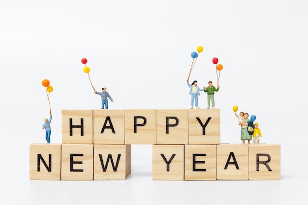 Gente en miniatura: familia feliz de pie en un bloque de madera Feliz año nuevo