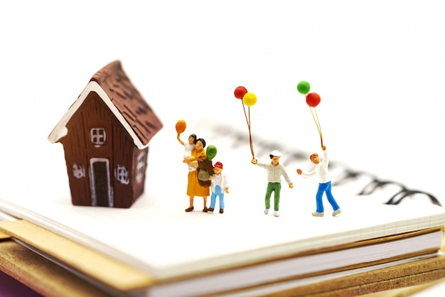 Gente en miniatura: familia y niños disfrutan con globos de colores y casa.