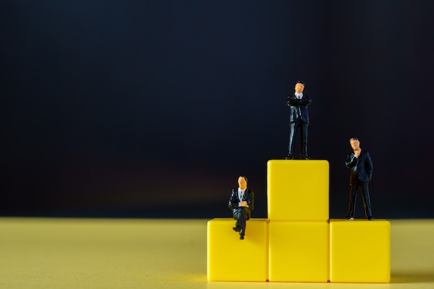 Gente en miniatura: figuras de pequeños empresarios de pie en el podio amarillo con superficie negra
