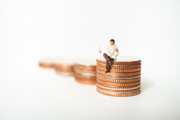 Gente miniatura, hombre leyendo periódico en monedas de pila