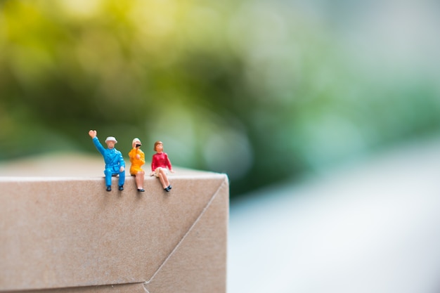 Gente miniatura, hombre y mujer que se sientan en la caja de papel usando como negocio y concepto social