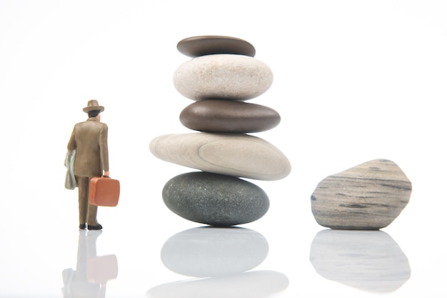 Gente en miniatura un hombre de negocios se encuentra cerca de una pirámide de piedra en un equilibrio de vida de fondo blanco