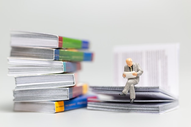 Gente en miniatura: hombre de negocios leyendo el periódico y sentado en el libro, concepto de conocimiento.