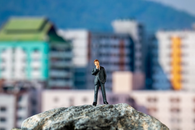 Gente en miniatura, hombre de negocios de pie sobre la roca con el edificio