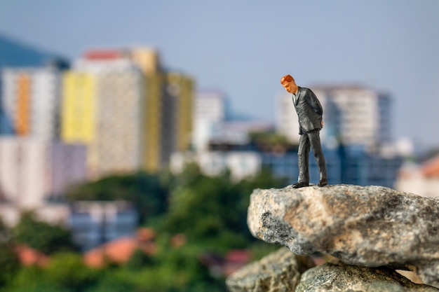 Gente en miniatura, hombre de negocios de pie sobre la roca con el edificio