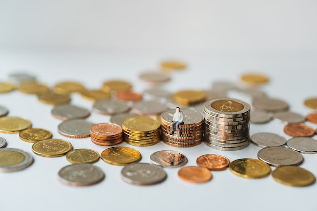 La gente miniatura, mujer joven que se sienta en monedas de la pila usando como negocio y concepto financiero