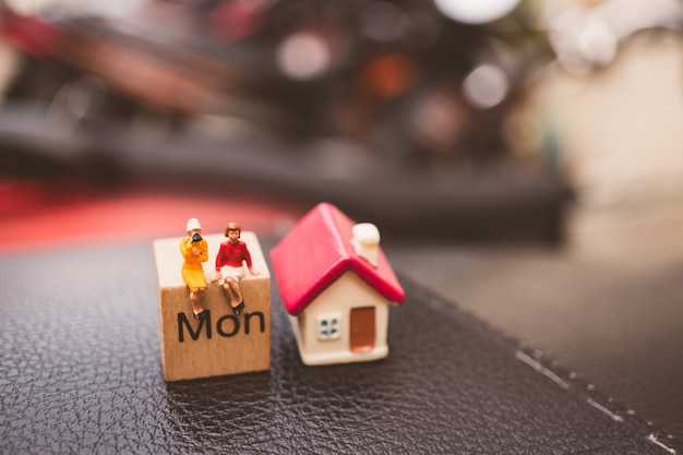 Foto gente miniatura, mujer pareja sentada en el calendario de bloque de madera con mini casa utilizando como negocio