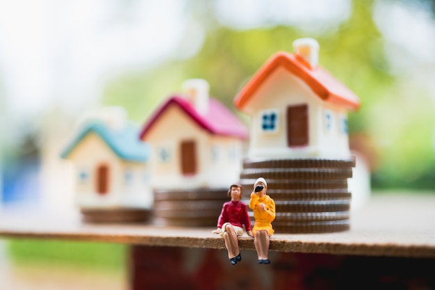 Gente miniatura, mujer de la pareja sentada delante de la mini casa en monedas de la pila, usando como negocio y