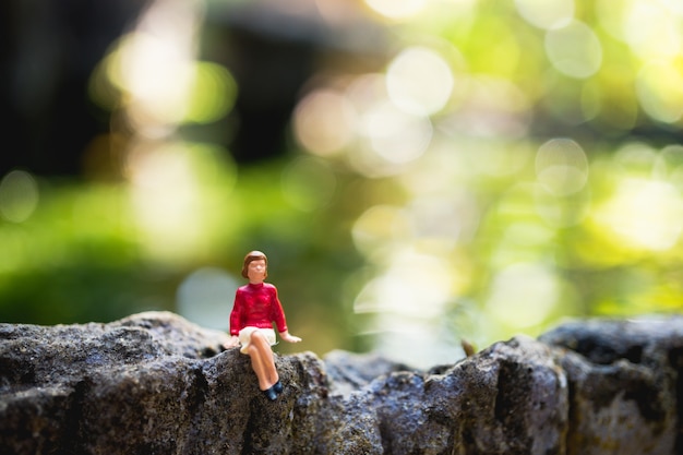 Gente miniatura, mujer sentada en la roca usando para el concepto de vacaciones