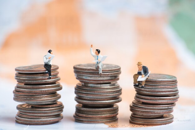 Gente miniatura de negocios sentado en la pila de monedas con fondo de mapa del mundo borrosa